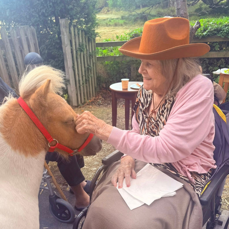 Female resident sat in wheelchair stroking small pony in the garden