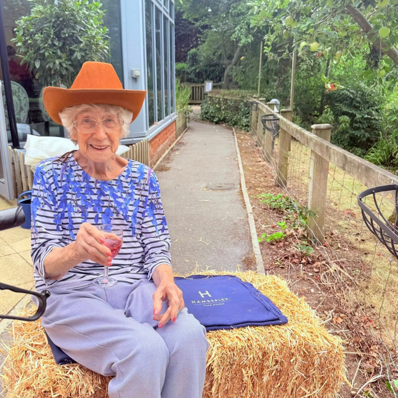 female resident with wine glass in hand sat on haybale in garden